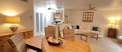 Un vaste espace de vie comprenant une table à manger, des chaises en osier, un canapé blanc et une cuisine en arrière-plan.