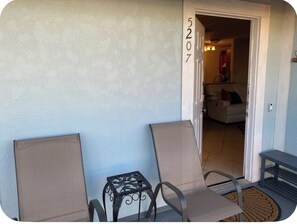 Eine Terrasse mit zwei Stühlen und einem kleinen Tisch, eine Tür mit der Nummer 5207 und ein Blick in ein Wohnzimmer.