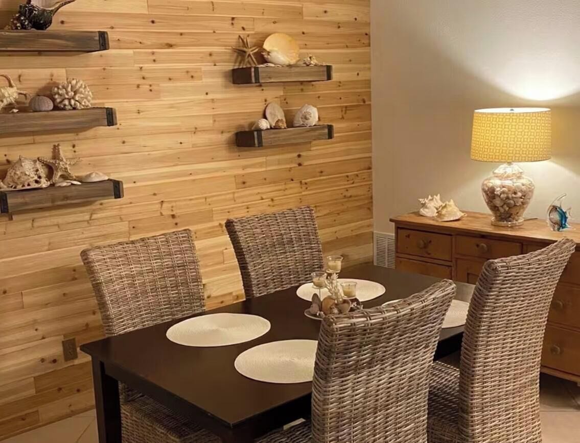 Ein Essbereich mit einer Holzwand, Korbstühlen, einem dunklen Tisch und dekorativen Muscheln.
