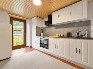 Une cuisine moderne avec des meubles blancs, un four encastré et une fenêtre donnant sur un jardin.