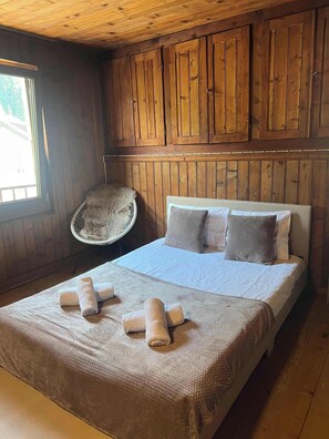 Une pièce aux murs lambrissés, contenant un lit, des oreillers, une chaise et une fenêtre.
