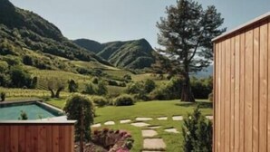 A wooden deck with a stone pathway leading to a pool, surrounded by a lush garden and a view of rolling hills.