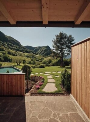 A wooden deck with a stone pathway leading to a pool, surrounded by a lush garden and a view of rolling hills.