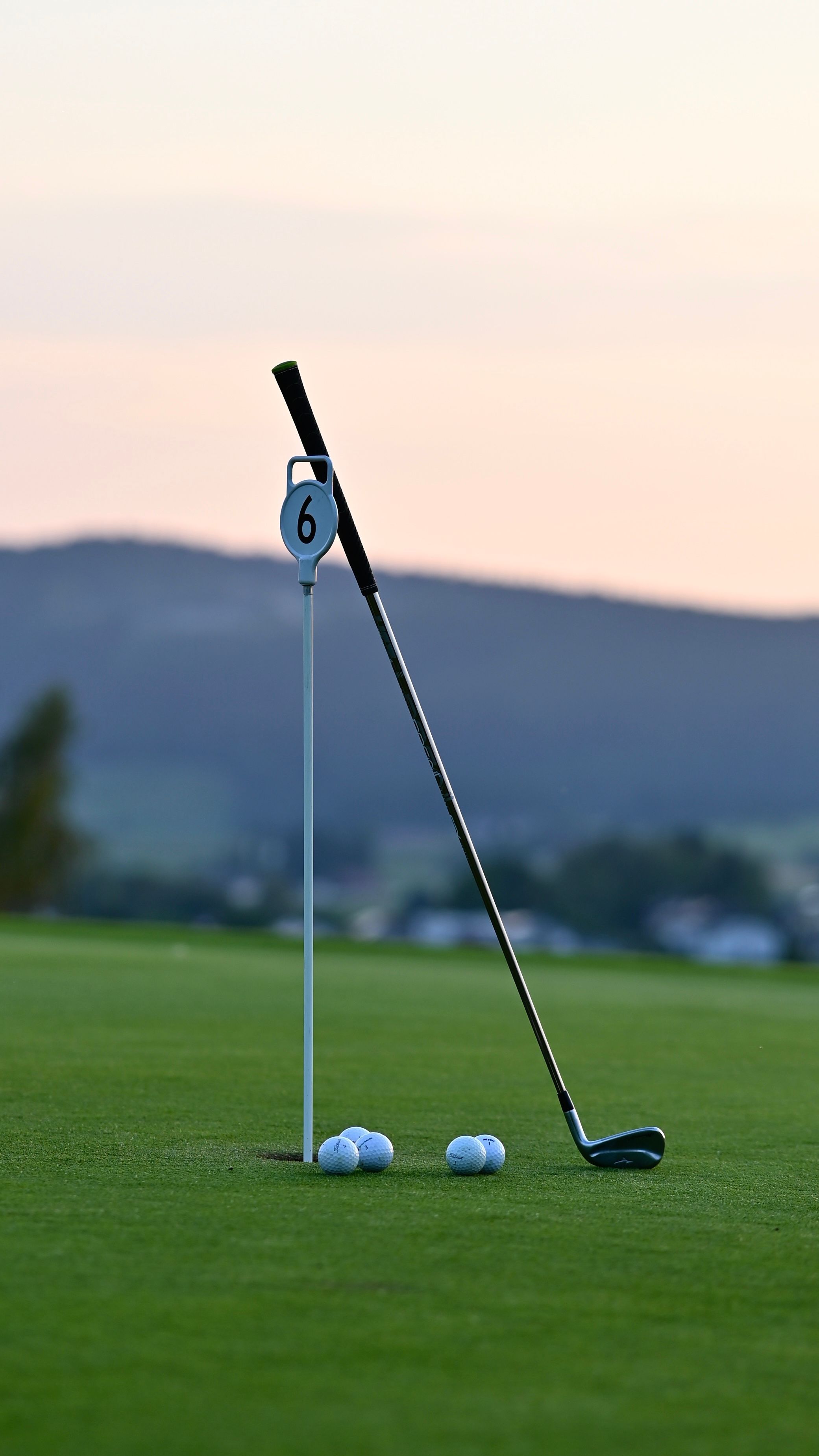 Un parcours de golf avec un mât de drapeau portant le numéro 6 et des balles de golf sur le green.