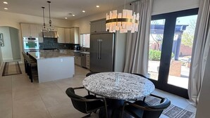 Et moderne køkken med en central ø, rustfrie hvidevarer og et spiseområde med et rundt bord og stole.