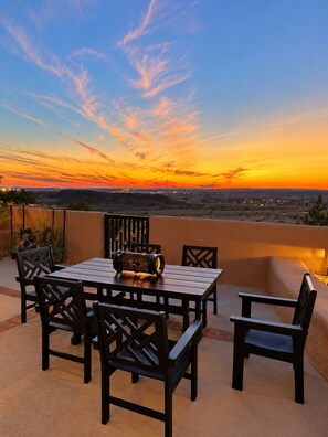 Eine Außenpatio mit Tisch und Stühlen, mit Blick auf eine Stadtlandschaft bei Sonnenuntergang.