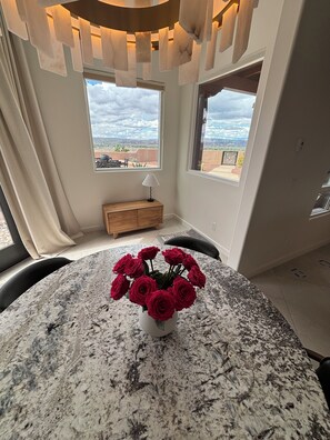 Ein Essbereich mit einem runden Marmortisch, einer Rosenvase und Blick auf die Wüste durch große Fenster.