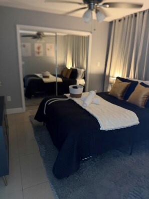 Quarto com cama, ventilador de teto e vista para outro cômodo.