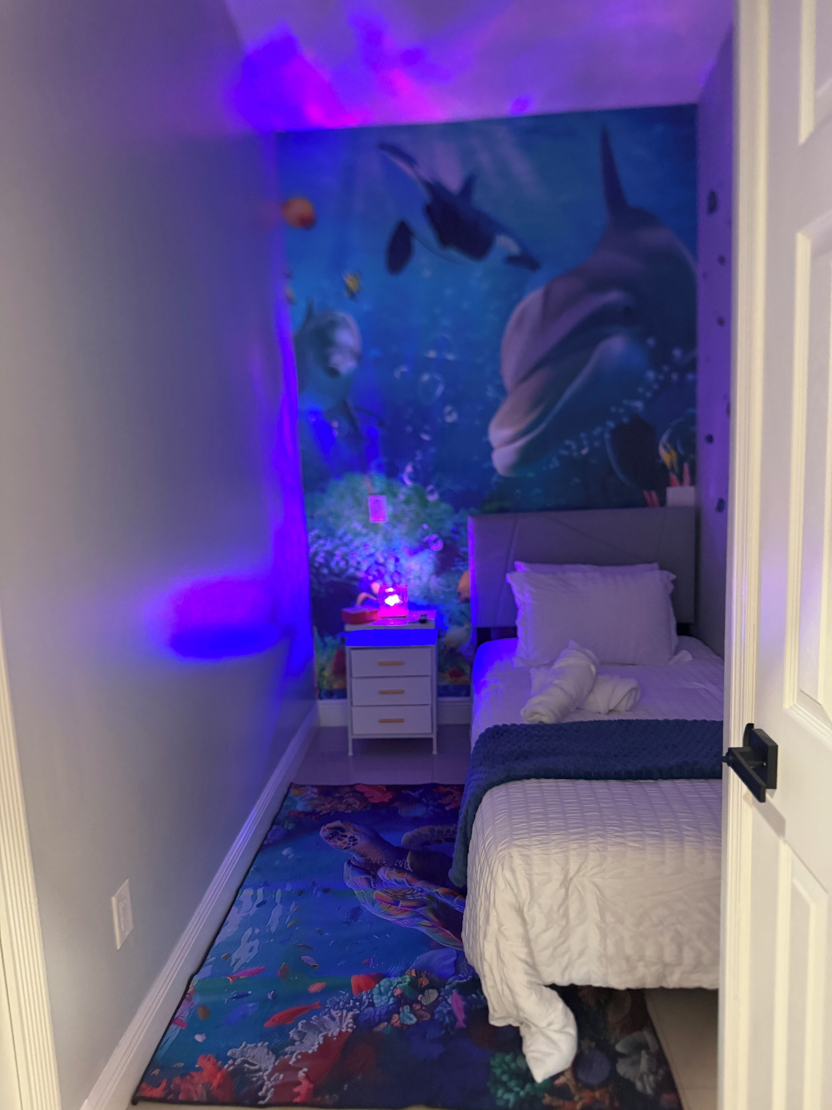 Ein Schlafzimmer mit Bett, Nachttisch, Wandgemälde und einem farbenfrohen Teppich.
