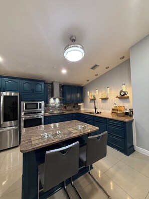 A modern kitchen with dark blue cabinets, stainless steel appliances, and a central island with bar stools. - Modern 3BR Tampa Home Near Airport & Stadium (Tampa)