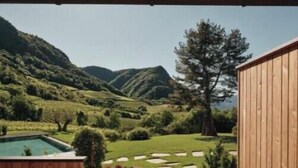 A wooden deck with a stone pathway leading to a pool, surrounded by a lush garden and a view of rolling hills.