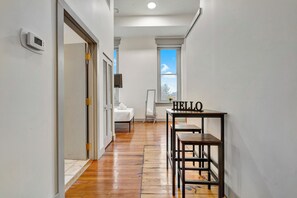 A hallway with a wooden floor, a white door, a 'HELLO' sign on a table, and a window with a view of the sky. - Executive Studio - Nearby Parking - Downtown - 3F (Louisville)
