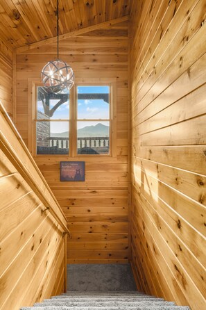 A wooden interior with a staircase leading to a window overlooking a mountain landscape. - Sleeps 8, Mountain View Hot Tub, Arcade, Pool Table, 2 Mi to Gatlinburg Parkway (Gatlinburg)