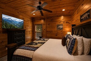 A wooden cabin bedroom with a bed, a ceiling fan, a television, and a sign reading 'Kibberation Station.' - Sleeps 8, Mountain View Hot Tub, Arcade, Pool Table, 2 Mi to Gatlinburg Parkway (Gatlinburg)