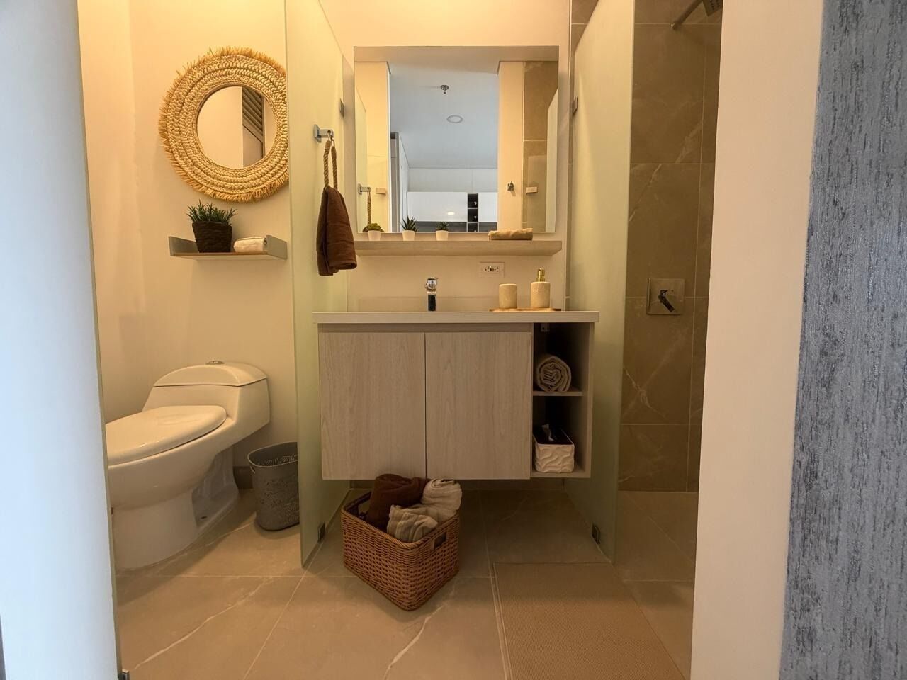 Een badkamer met toilet, een wastafel met spiegel erboven, een handdoekrek en een mand op de vloer.