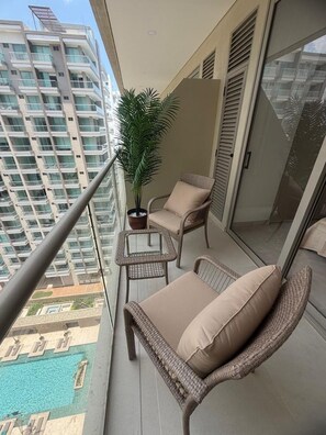 A balcony with wicker furniture, a potted plant, and a view of a swimming pool and high-rise buildings. - Apartment near the ocean at Bello Horizonte 1416 (Santa Marta)
