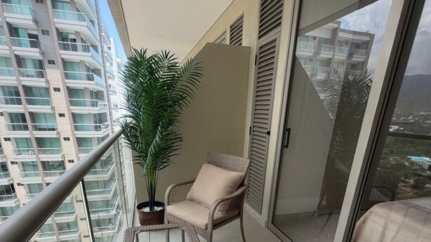 Uma varanda com móveis de vime, um vaso de planta e vista para edifícios altos.