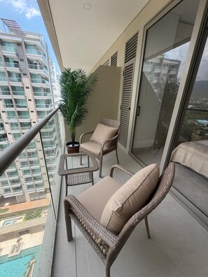 A balcony with wicker furniture, a potted plant, and a view of high-rise buildings. - Apartment near the ocean at Bello Horizonte 1416 (Santa Marta)