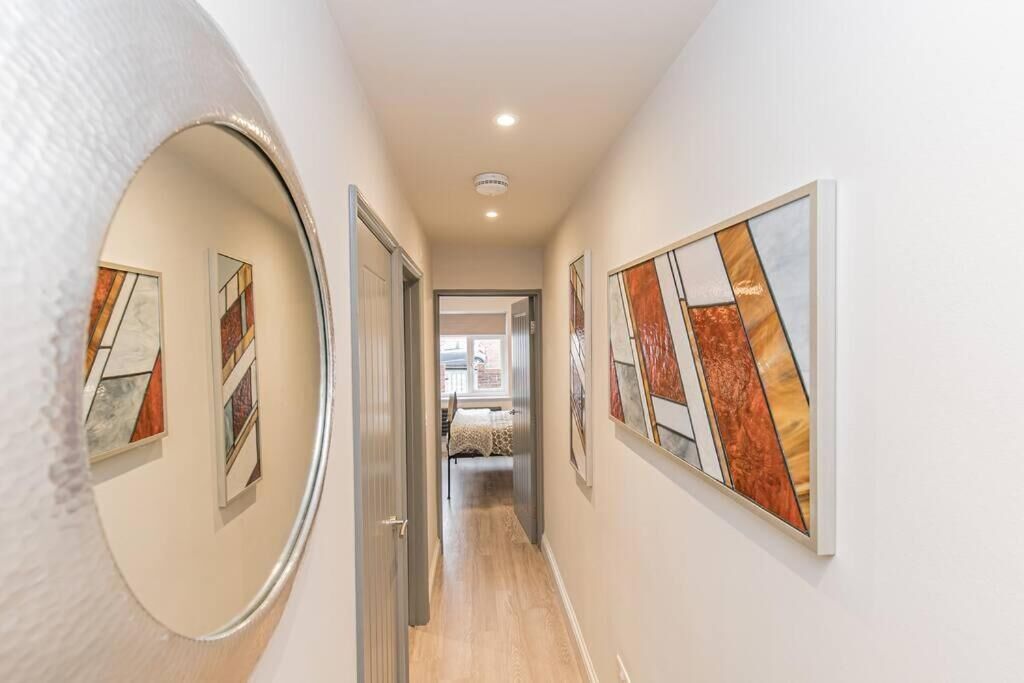 A hallway with artwork on the walls, a door on the left, and a bed in the background.