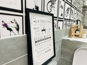 Ein Badezimmer mit gefliesten Wänden, einem gerahmten Schild mit Badezimmerregeln und einer Holzkiste mit Toilettenartikeln.