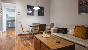Uma sala de estar moderna com uma mesa de centro de madeira, um sofá com almofada decorativa, e um espaço de jantar com cadeiras e uma mesa de vidro.