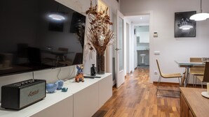 Uma cozinha moderna com uma grande televisão de tela plana, uma bancada branca e um espaço de refeições com uma mesa e cadeiras de madeira.