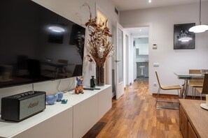 A modern kitchen with a large flat-screen TV, a white countertop, and a dining area with a wooden table and chairs. - Fast Wi-Fi - Rooftop - 3 bedrooms - Sagrada Metro Station (Barcelona)