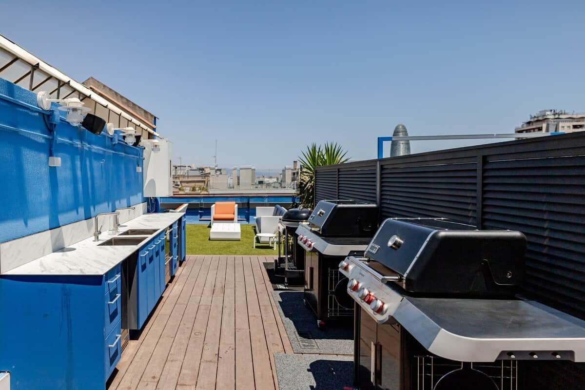 Un bar en la azotea con una zona de cocina azul, asientos al aire libre y varias parrillas.