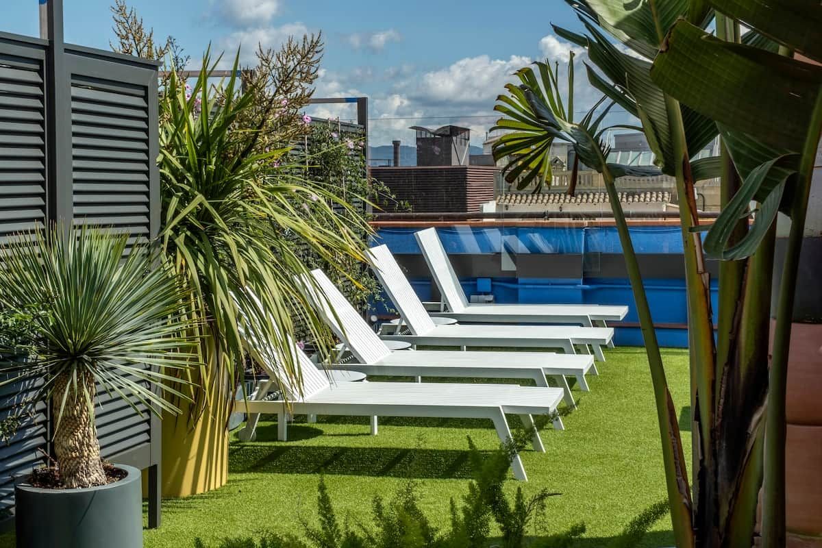 Zona de piscina al terrat amb gandules blanques i plantes tropicals.
