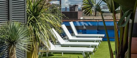 A rooftop pool area with white lounge chairs and tropical plants.