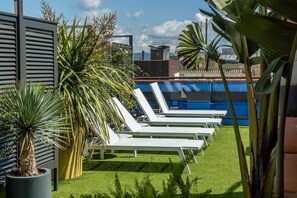 Un espace piscine aménagé sur le toit, avec des chaises longues blanches et des plantes tropicales.