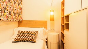 Quarto com cama, luminária de cabeceira, lixeira e parede com cortina estampada.