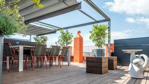 Terraço no telhado com mesa e cadeiras, plantas em vasos e uma escultura decorativa.