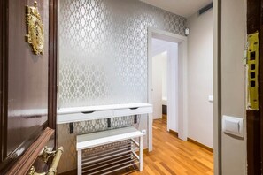 Un couloir avec un mur orné de motifs, un banc blanc et une porte dotée d’une poignée en laiton.