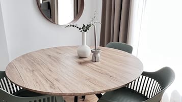Ein runder Esstisch mit Holzbeschichtung, umgeben von vier Stühlen in Grün und Schwarz. Auf dem Tisch steht ein weißer Blumenvasen mit einer Pflanze.