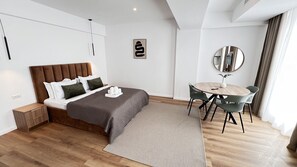A modern hotel room with a bed, bedside table, a round dining table with chairs, a mirror, and a wall-mounted artwork. - AeroGrey Residence Apartments (Tunari)