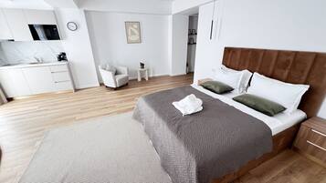 A modern bedroom with a large bed, a bedside table, a nightstand, a small round table, and a chair.