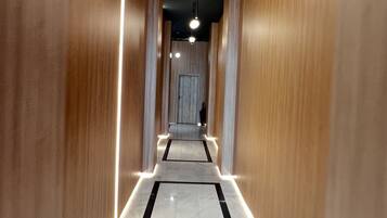 A corridor with wooden walls, a marble floor, and ceiling lights.