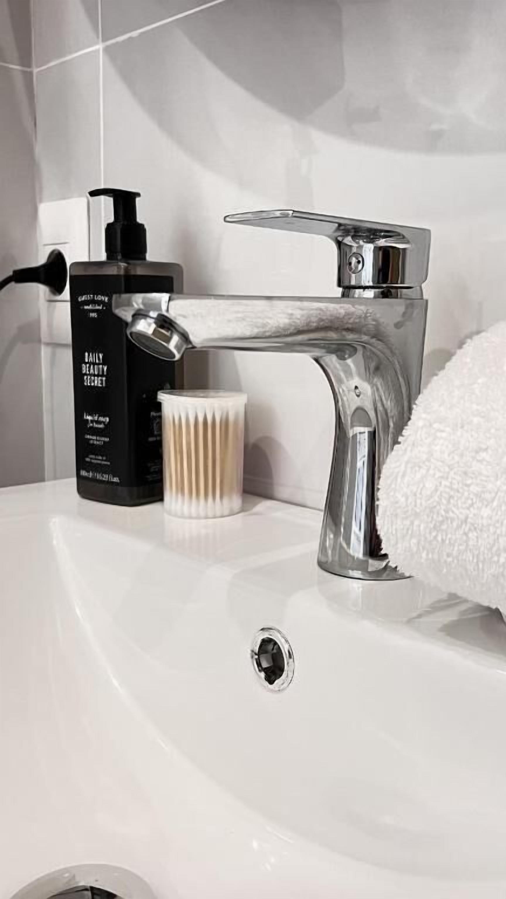 Ein Waschbecken mit chromfarbenem Wasserhahn, einer Lotionflasche und einem weißen Handtuch.