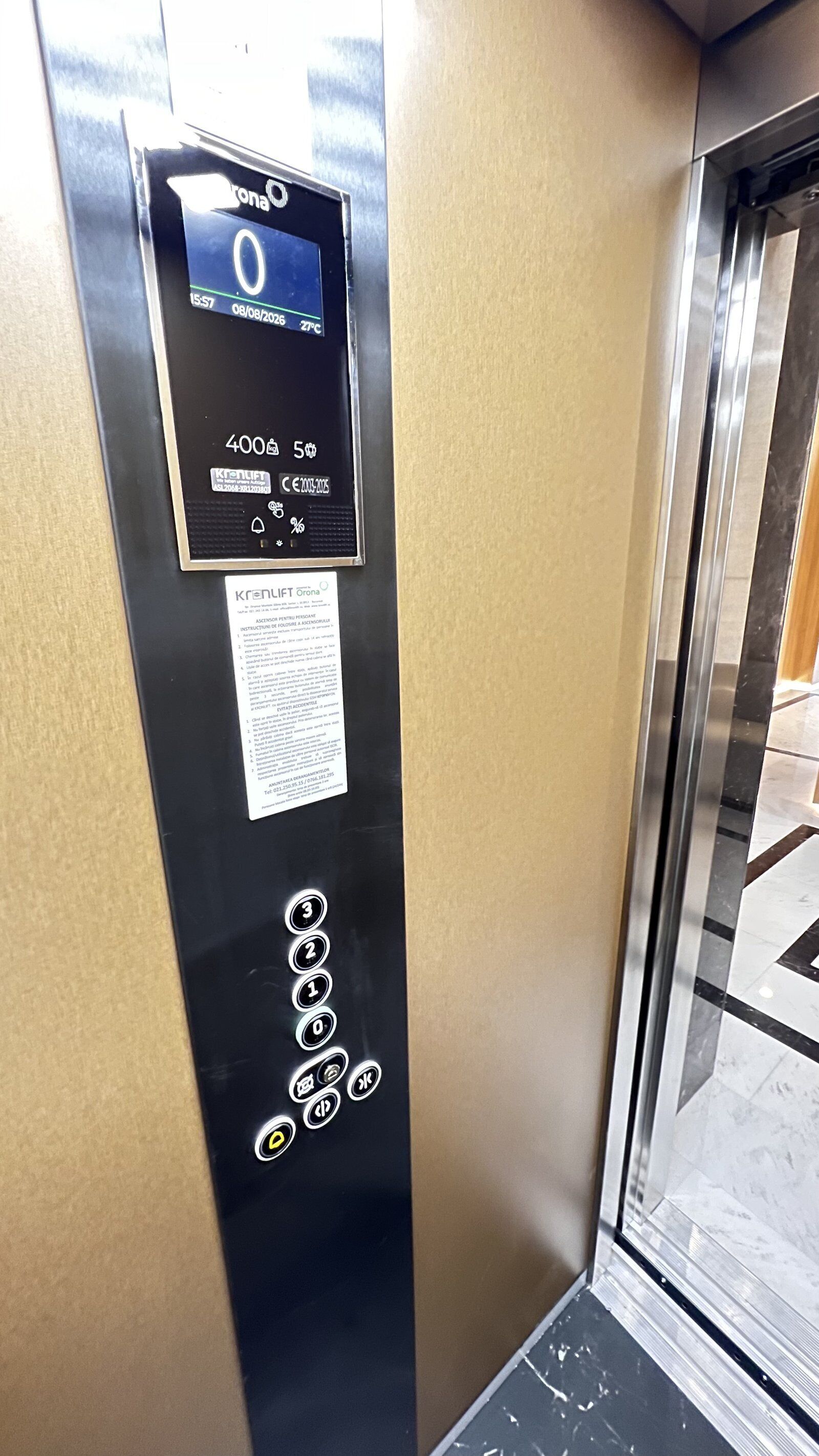 Een bedieningspaneel van een lift met een digitaal scherm, instructies voor noodgevallen en knoppen voor verdiepingen.