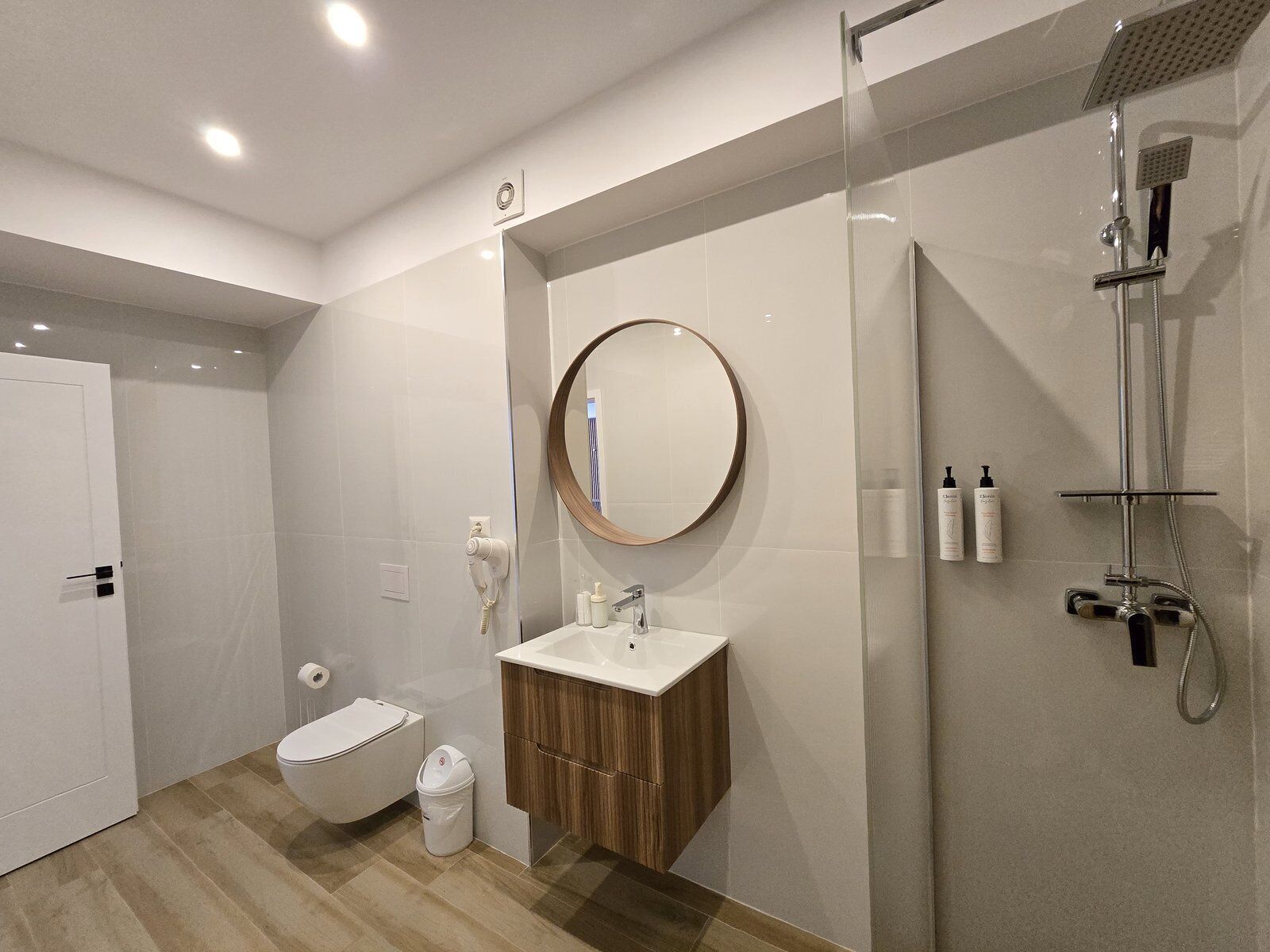 A modern bathroom with a toilet, sink, mirror, and shower.