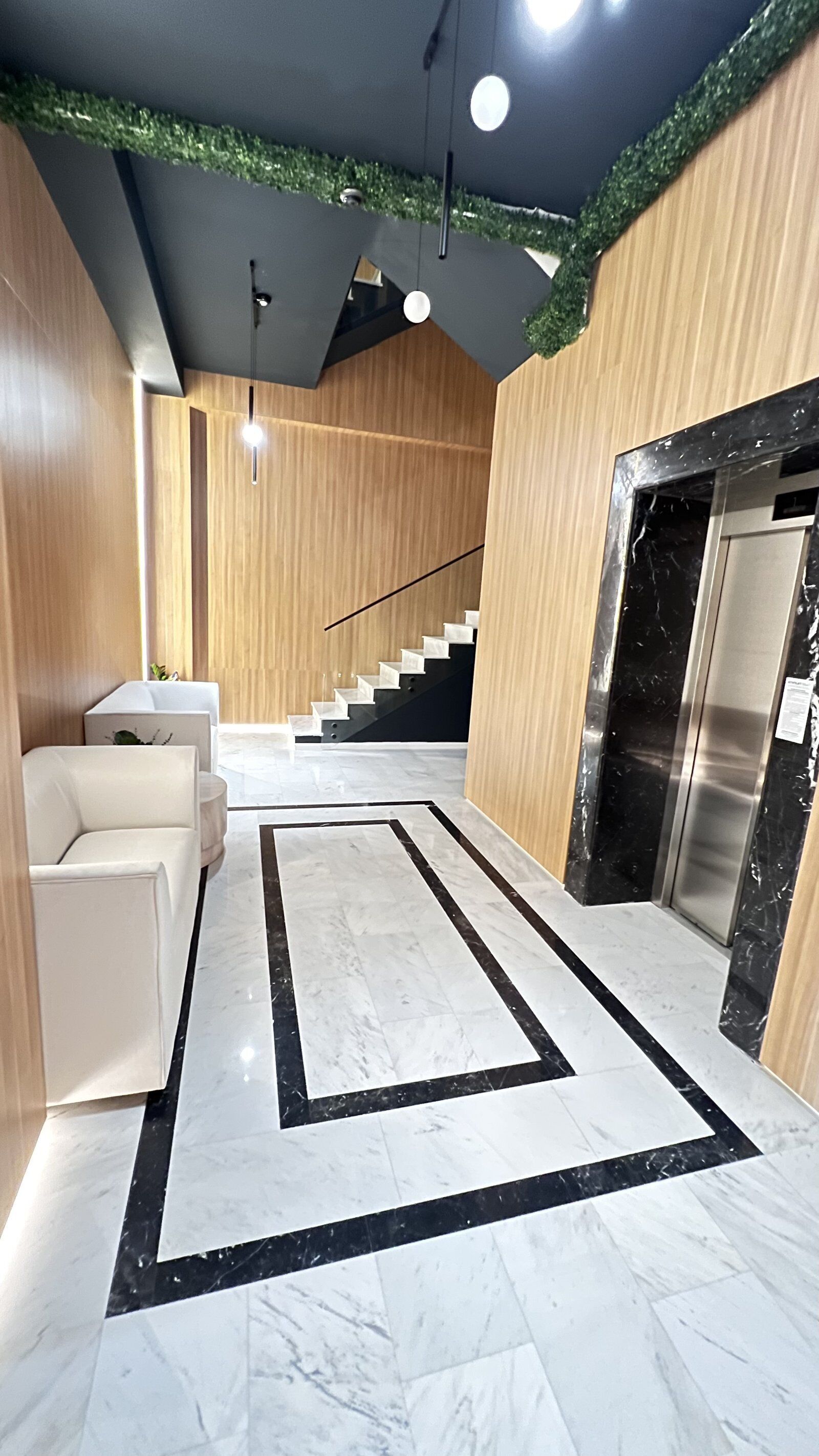 A modern interior with a marble floor, a staircase, and a reception area with a reception desk and seating.