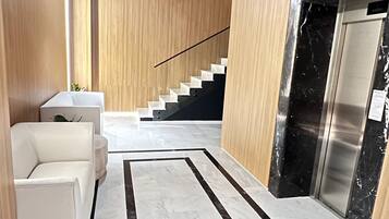 A modern interior with a marble floor, a staircase, and a reception area with a reception desk and seating.