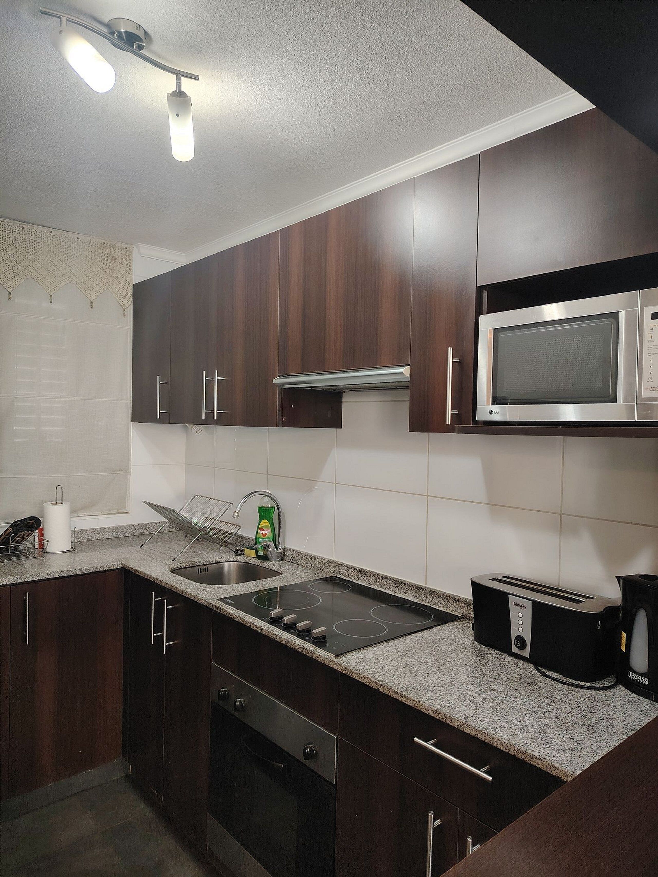 Una cocina con armarios de madera oscura, un microondas de acero inoxidable, un horno empotrado, una estufa a gas y un tostador.