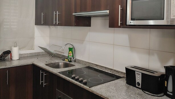 Una cocina con armarios de madera oscura, un microondas de acero inoxidable, un horno empotrado, una estufa a gas y un tostador.