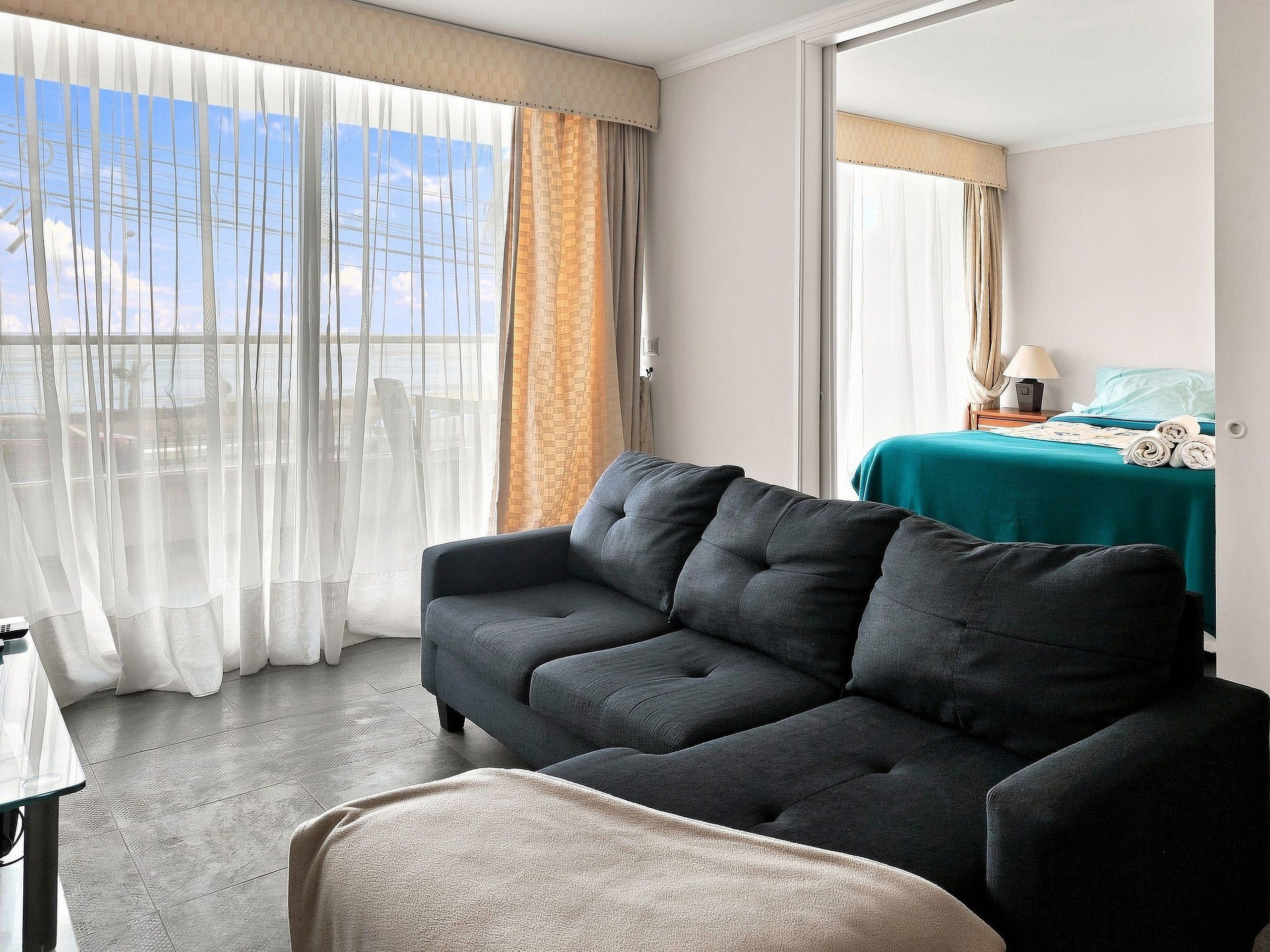 Ein Hotelzimmer mit einer Couch, einem Bett mit türkisblau versteckter Bettdecke und Blick aus dem Fenster.