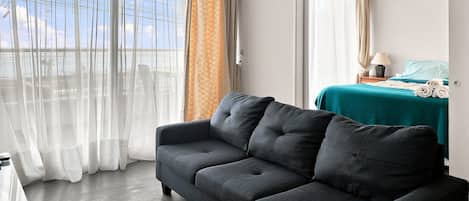 Una habitación de hotel con sofá, cama con colcha color turquesa y vistas a través de la ventana.