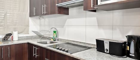 A kitchen with dark wooden cabinets, a stainless steel sink, a microwave, a toaster, and a kettle.