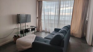 Una sala de estar con sofá, televisor de pantalla plana y un mueble bajo de vidrio.