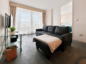 A modern living room with a sofa, a glass coffee table, a television, and a window with curtains. - Oceana Suites Neohaus (La Serena)